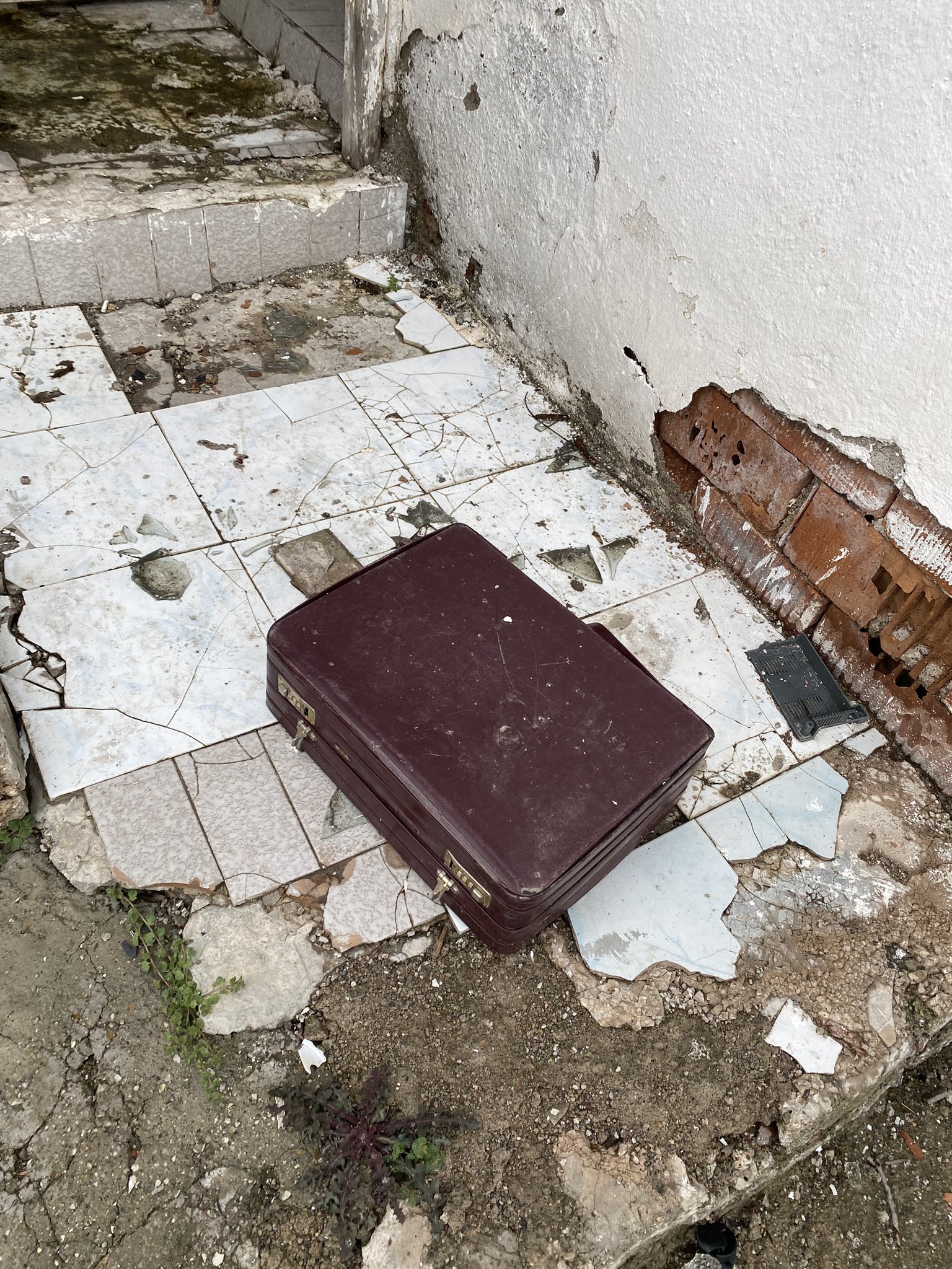 A suitcase left on broken tiles beside a peeling wall